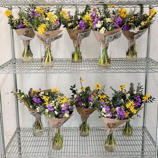 A group of bouquets made by Bloom Sacramento on a shelf in a flower cooler