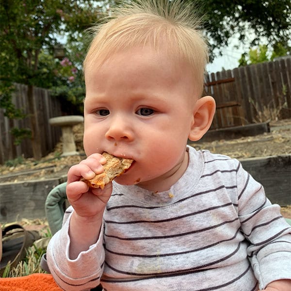 Baby eats pizza crust while sitting outside
