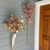 Two dried flower brooms made by Bloom Sacramento hang by a front door