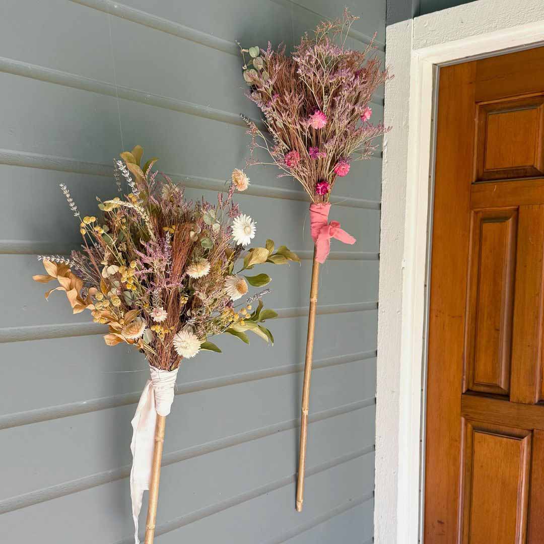 Two dried flower brooms made by Bloom Sacramento hang by a front door