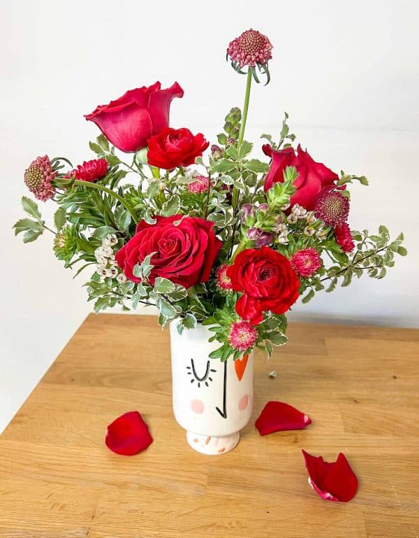 Arrangement of red roses and other flowers in white vase