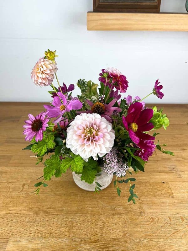 A flower arrangement in a vase sits on a wooden table