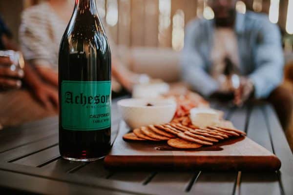 A bottle of wine reads Acheson Wine Company, sitting on table next to crackers