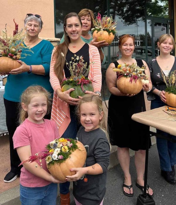 Group of people hold pumpkins decorated with dried flowers and other additions.