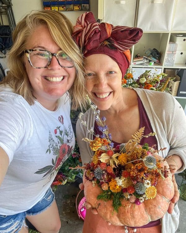 Two people pose for a photo in front of a pumpkin decorated with dried flowers and other additions, created by Bloom Sacramento