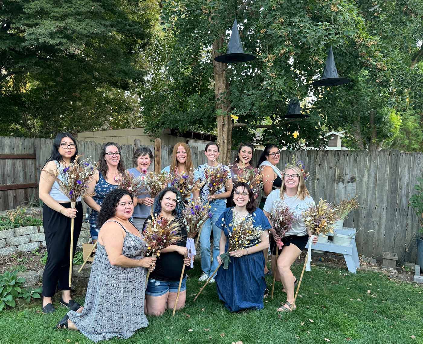 People pose for a photo after creating witch's brooms at a workshop hosted by Bloom Sacramento
