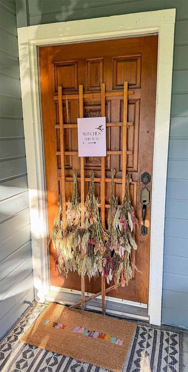 Dried flowers hang in front of door with sign saying "witches this way" with an arrow pointing to the right
