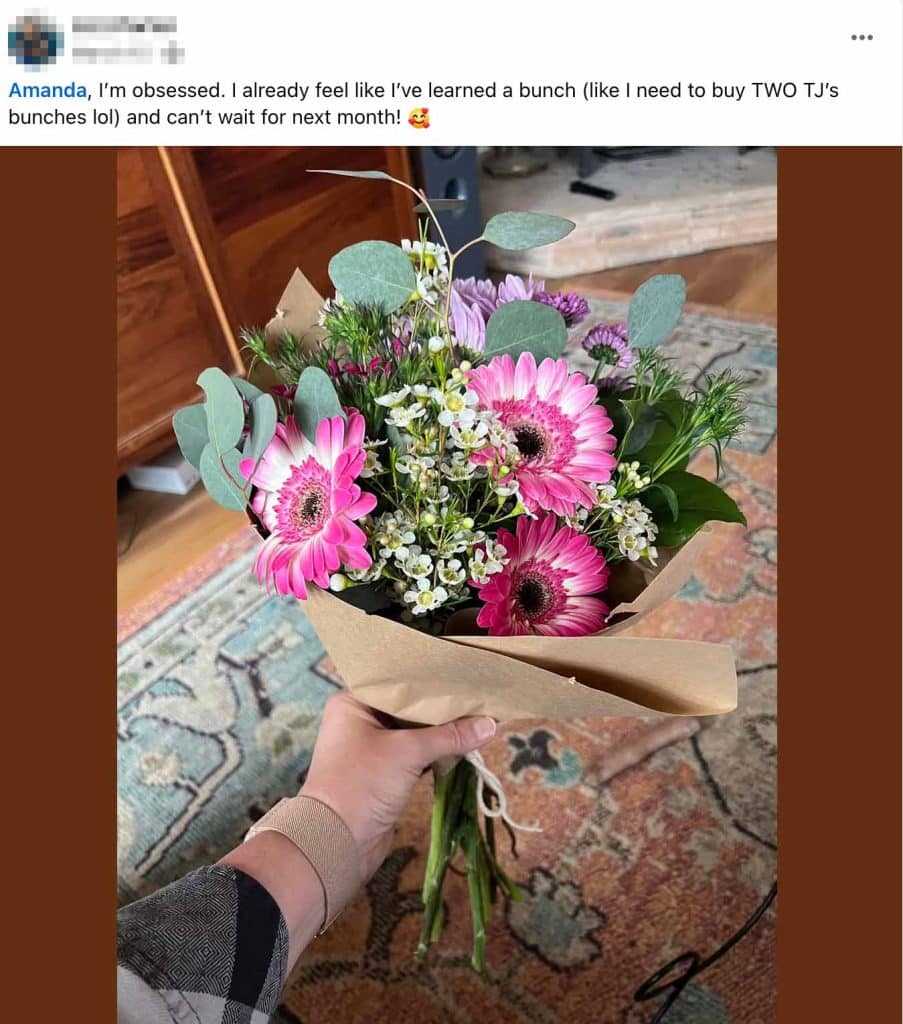 Social media post showing a hand holding a beautiful flower bouquet wrapped in brown paper. The bouquet contains pink gerbera daisies, white small flowers, purple blooms, and eucalyptus leaves. The post text reads: "Amanda, I'm obsessed. I already feel like I've learned a bunch (like I need to buy TWO TJ's bunches lol) and can't wait for next month! 🥰" The photo is taken indoors on a patterned rug.