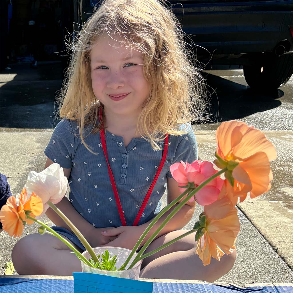 Young girl sits with jar of flowers for sale