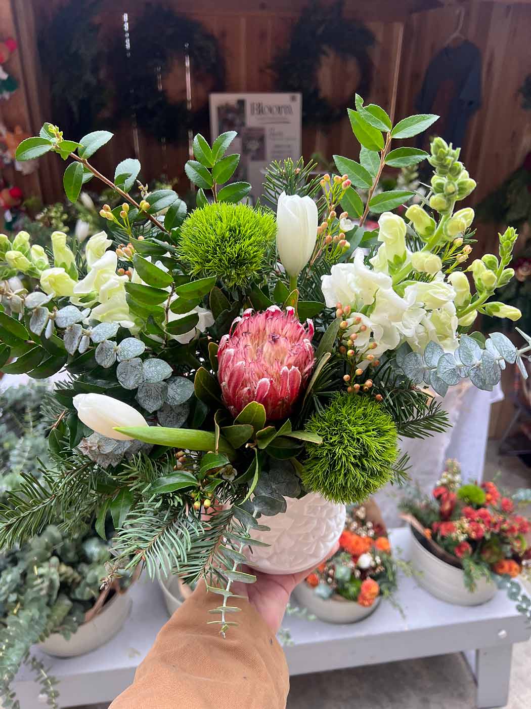 A hand holds a vase with winter flowers in it