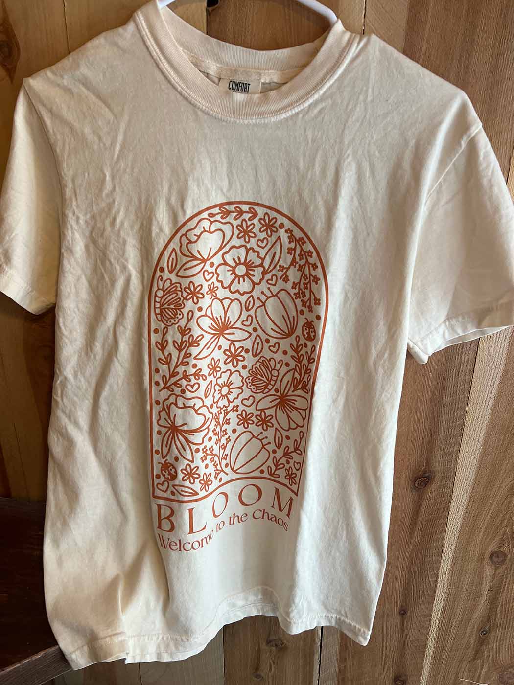 White shirt with design that reads "Bloom - welcome to the chaos"