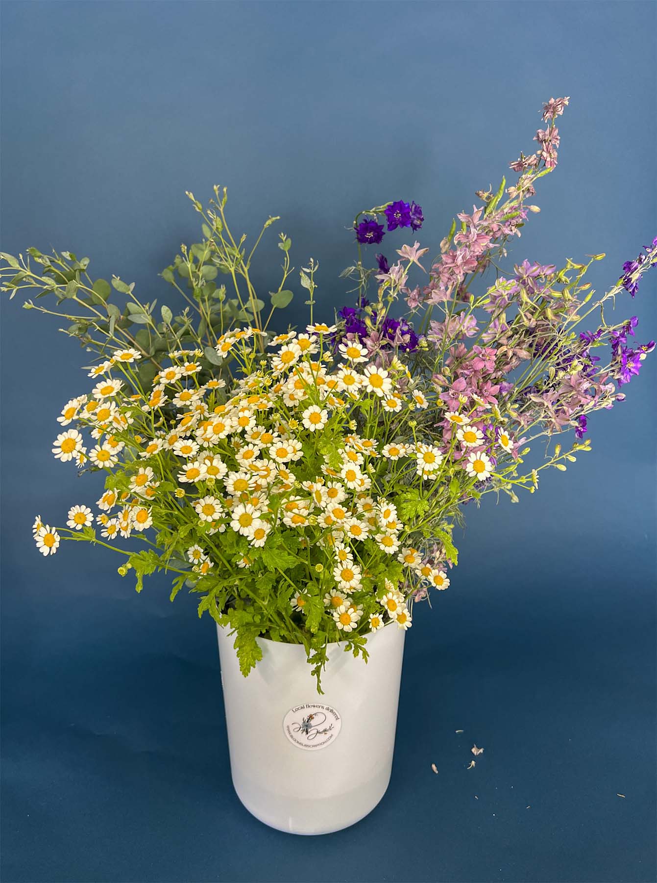 A bucket of flowers grown by Bloom Sacramento photographed against a blue background